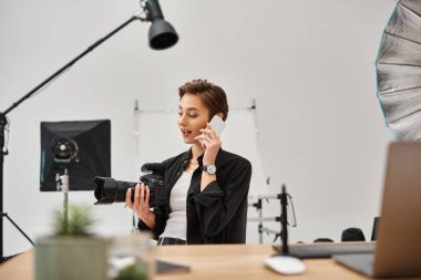 Elinde kamerayla cep telefonuyla konuşan neşeli, çekici bir kadın fotoğrafçı.