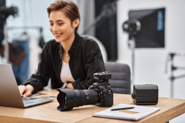 Masadaki modern kameraya odaklan. Stüdyodaki neşeli profesyonel kadın fotoğrafçının yanına.