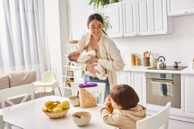 Mutlu, çekici bir anne, yürümeye yeni başlayan çocuğuyla, modern ebeveynlikle kahvaltı yapıyor.