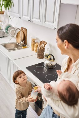 loving happy mother in housewear spending time with her toddler and newborn sons during breakfast clipart