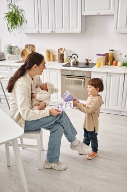 Sevimli çocuk, yeni doğan erkek kardeşi Anneler Günü 'nü elinde tutarken annesine hediye ve kartpostal veriyor.