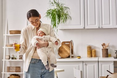 Mutlu ve sevgi dolu bir anne kucağında yeni doğmuş bebeğiyle elinde portakal suyu, modern ebeveynlik