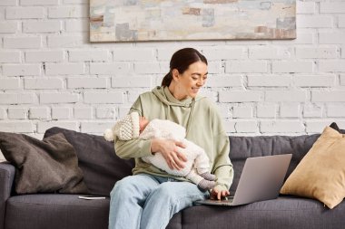 good looking jolly mother in casual attire having videocall and holding her newborn baby boy clipart
