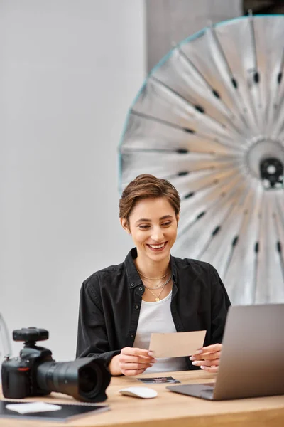 stock image cheerful female photographer in casual attire sitting at table and looking at photos in her hands