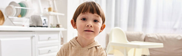 adorable toddler boy in comfy homewear looking at camera during breakfast on kitchen, banner