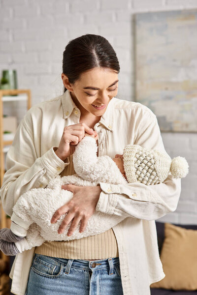 attractive cheerful mother in homewear holding lovingly her newborn baby boy, modern parenting