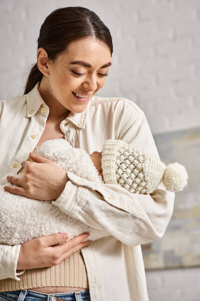 beautiful cheerful mother in homewear holding lovingly her newborn baby boy, modern parenting