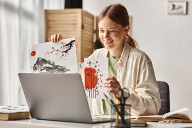 Çalışırken ve bilgisayarına bakarken sanat eserlerini gösteren mutlu genç bir kız.