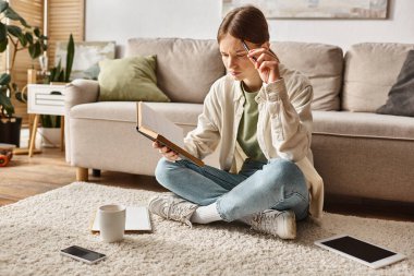 smart teen girl reading book while doing homework among devices and cup of tea, generation z clipart