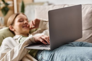 Dizüstü bilgisayara odaklan, mutlu genç nesil z kızı kanepede uzan ve bilgisayarını evde kullan.