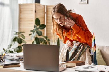 Evde internetten ders çalışan genç bir kız masasında Gurur Igbtq bayrağının yanına telefon ediyor.