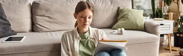 一个多愁善感的少女 带着耳机和数码平板电脑 一面横幅 在沙发边看书本 — 图库照片
