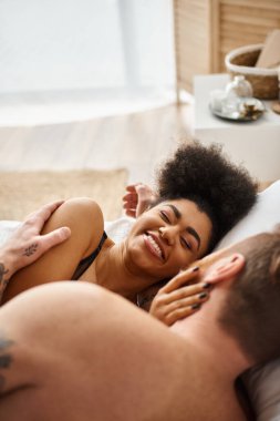 Mutlu Afro-Amerikan kadın dövmeli erkek arkadaşıyla yatakta yatarken gülümsüyor.