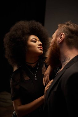 Kıvırcık saçlı Afro-Amerikalı kadın sakallı, dövmeli erkek arkadaşını baştan çıkarıyor.