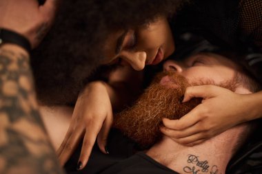 Kıvırcık saçlı, sakallı ve dövmeli kızıl saçlı erkek arkadaşını baştan çıkaran Afro-Amerikan kadını.
