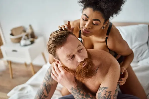sexy diverse couple, african american woman seducing her tattooed man on a bed in a bright room