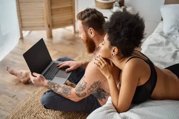 stock image interracial couple lying on bed and enjoying cozy moment while watching movie on laptop together
