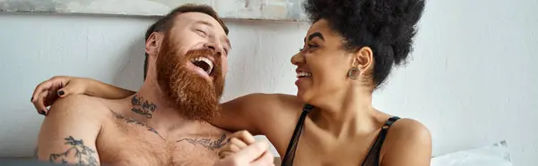 happy and tattooed man without shirt laughing with curly african american girlfriend, banner