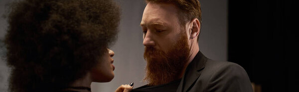 curly african american woman in dress pulling blazer of bearded man during date, sexy couple banner
