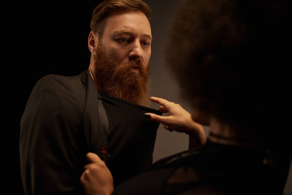african american woman in dress pulling blazer of bearded man during date, sexy couple on date