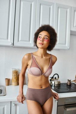 Hayalperest Afro-Amerikan kadın sütyenli pembe bantlı modern mutfakta duruyor.