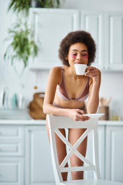İç çamaşırlı ve sabah kahvesini koklayan mutlu Afro-Amerikan kadın.
