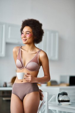 İç çamaşırlı ve fincanda kahve içen mutlu Afro-Amerikalı kadın.