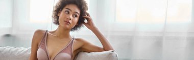Thoughtful young african american woman lounging in lingerie on a sofa at home, horizontal banner clipart