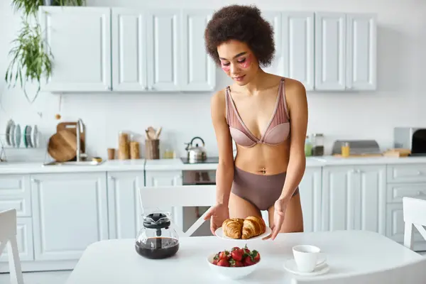 stock image young african american woman in lingerie serving croissants and strawberries for breakfast