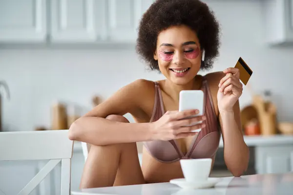 ポジティブなアフリカ系アメリカ人女性がキッチンでクレジットカードとスマートフォンでオンラインショッピング — ストック写真