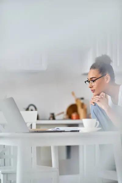 stock image focused and young african american woman in glasses working from home remotely on her laptop