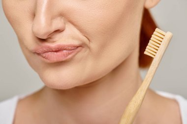 30 'lu yaşlarda, elinde gri arka planda bambu bir diş fırçası tutan endişeli bir kadının görüntüsü.