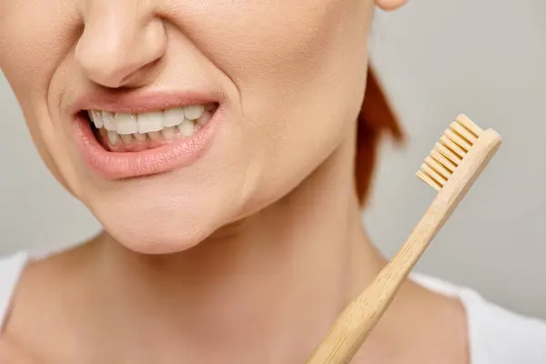 stock image cropped shot of displeased woman in 30s with white healthy teeth holding a bamboo toothbrush