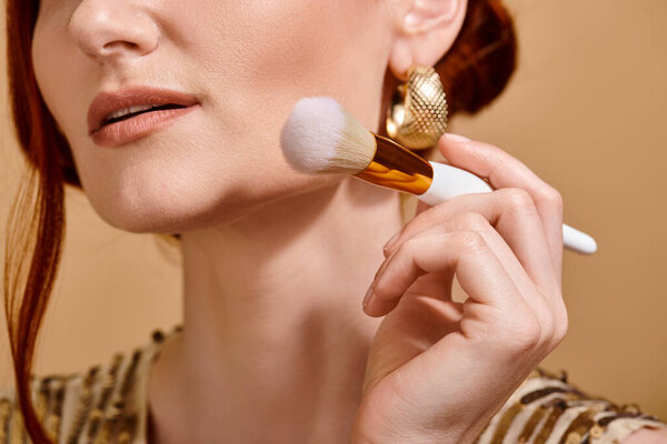 cropped redhead woman in gold earring holding makeup brush for liquid foundation application