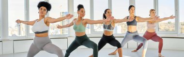 Spor giyim sektöründe Afro-Amerikan bayan eğitmenle pilates yapan genç kadınların bayrağı.