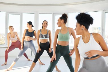 Spor kıyafetleri içinde bir grup mutlu kadın Afrikalı Amerikalı kadın eğitmenle pilates yapıyor.