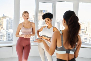 Bayan pilates eğitmeni dersten önce spor giyim ve spor salonunda neşeli çoklu etnik kadınlarla konuşuyor.