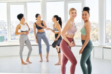 Spor giyimli, neşeli, çok kültürlü kadınlar pilates dersinden önce sohbet ediyorlar. Kameraya bakın.