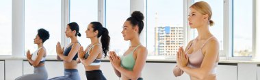 Parlak stüdyoda yoga yapan, dua eden elleri olan beş kültürlü kadının afişi.