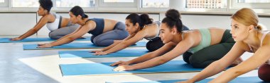 20 'li yaşlarda beş çok kültürlü kadın grubu minderlerde yoga yaparken geriliyor.