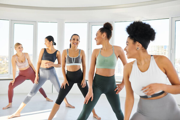 group of happy diverse women in sportswear practicing pilates with female african american trainer