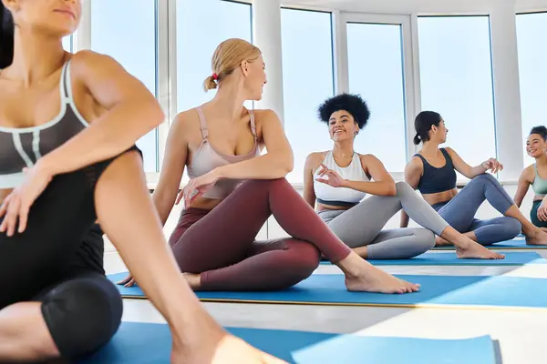 stock image Group of flexible and smiling multicultural women sitting in half lord of fishes yoga pose on mats