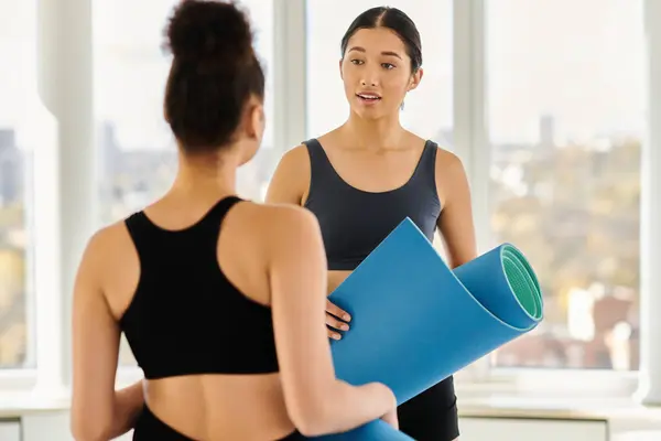 young asian woman in her 20s looking at her african american woman with fitness mat after workout