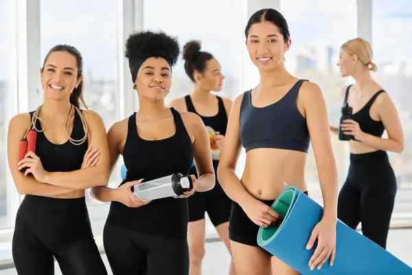 stock image cheerful interracial sportswoman in active wear looking at camera after workout in pilates studio