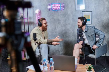 İyi görünümlü röportajcı ve kulaklıklı konuğu stüdyoda sorular ve podcast hakkında konuşuyorlar.