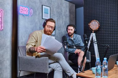 Çok çalışan kızıl saçlı röportajcı podcast sırasında genç konuğuyla ana soruları tartışıyor.