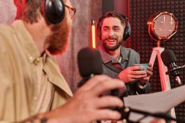 Podcast sırasında kulaklık takıp konuşan iki sakallı yakışıklı adam, kahve fincanı.