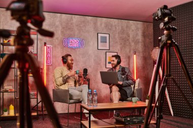 İyi görünümlü sakallı, kulaklıklı kahve içen ve podcast sırasında etkin bir şekilde konuşan adamlar.