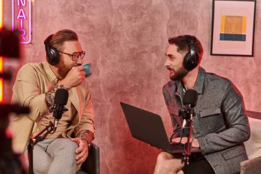 İyi görünümlü sakallı, kulaklıklı kahve içen ve podcast sırasında etkin bir şekilde konuşan adamlar.
