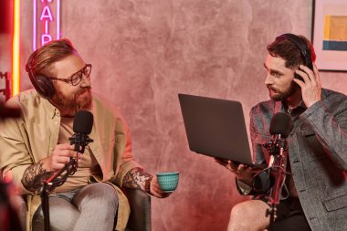 İnternet yayını sırasında kahve ve dizüstü bilgisayarla poz veren sıradan giyinmiş yakışıklı adamlar.